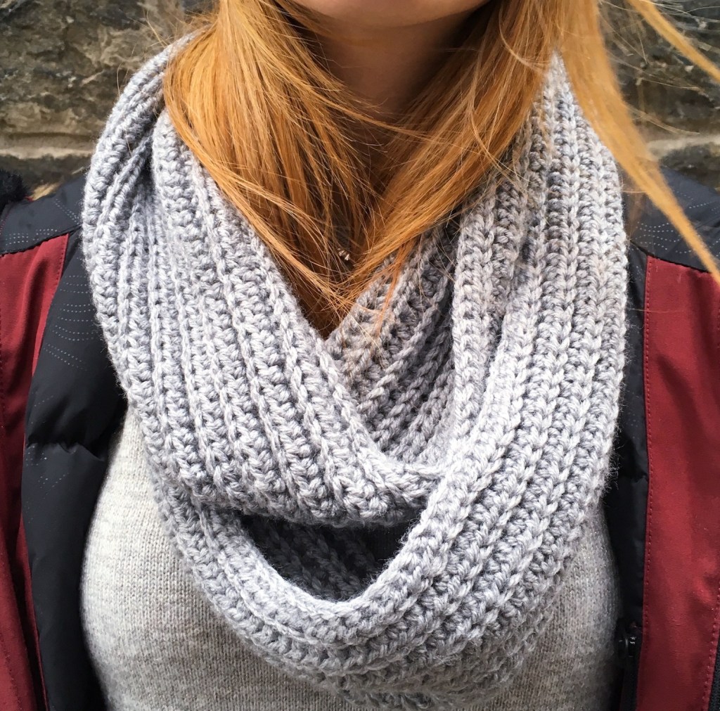 Picture of a female's torso wearing a grey crochet infinity scarf and red winter jacket.